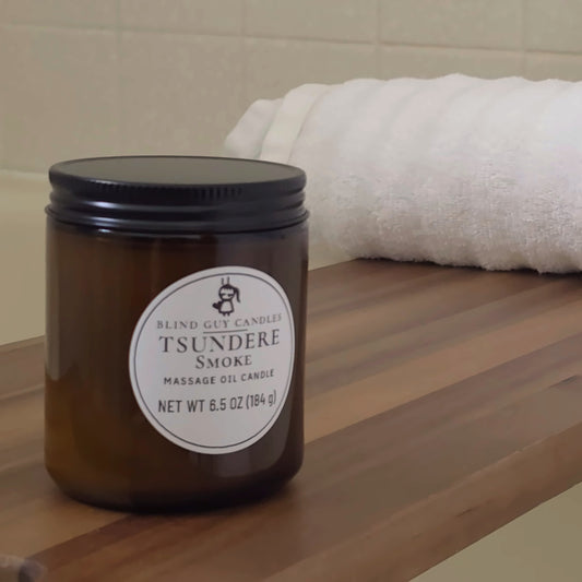 Tsundere Smoke massage oil candle on a wooden bath tray beside a white towel