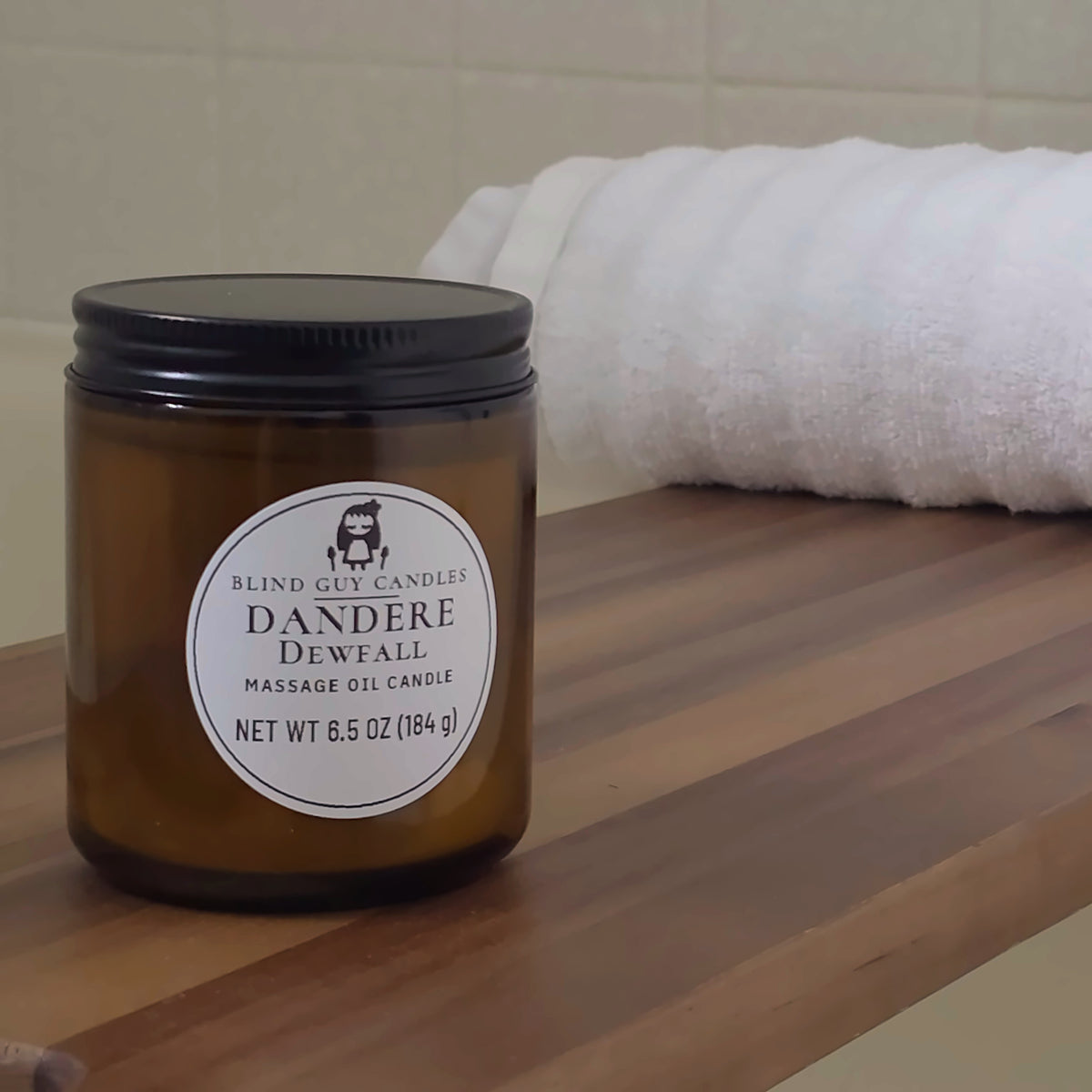 Dandere Dewfall massage oil candle on a wooden bath tray beside a white towel