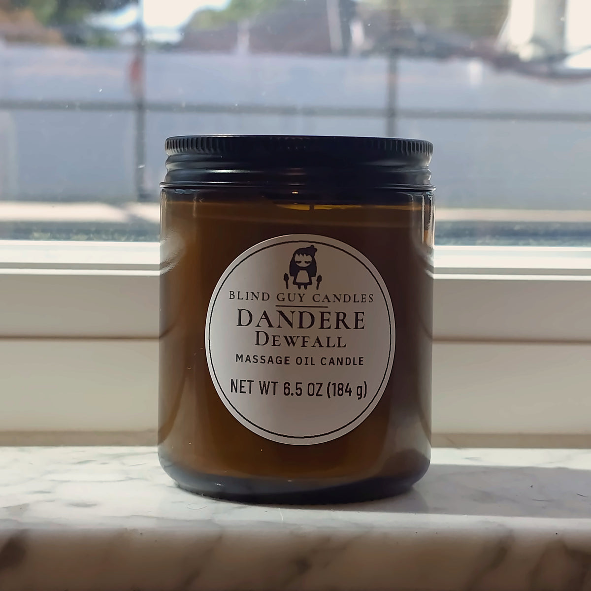 Dandere Dewfall massage oil candle in its amber jar on a marble windowsill in daylight