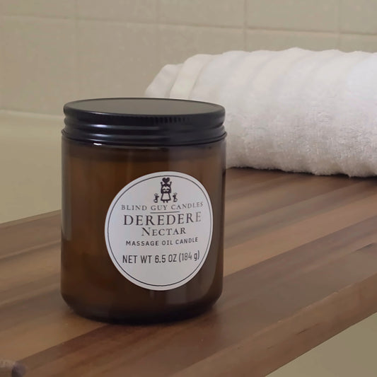 Deredere Nectar massage oil candle on a wooden bath tray beside a white towel