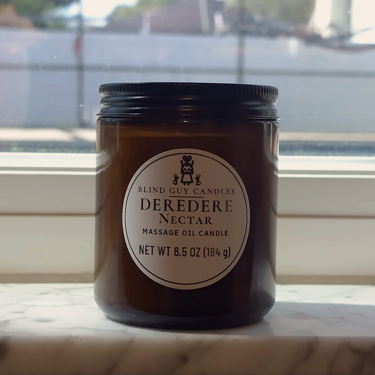 Deredere Nectar massage oil candle in its amber jar on a marble windowsill in daylight